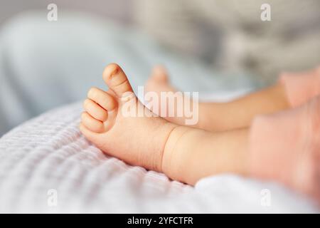 Gros plan sur les pieds minuscules du nouveau-né dans des vêtements roses, reposant confortablement sur une couverture légère douce. Banque D'Images