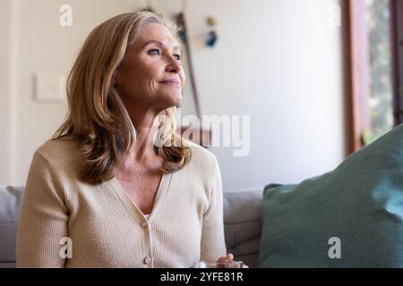 Femme senior souriante se relaxant sur le canapé à la maison, profitant d'un moment paisible Banque D'Images