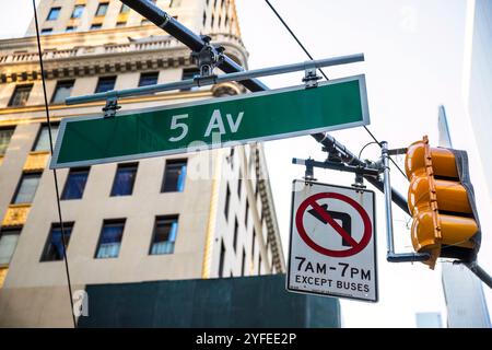 Un panneau indiquant Fifth Avenue à New York City est monté au-dessus d'un feu de circulation, ainsi qu'un panneau indiquant les heures d'ouverture restreintes. Banque D'Images