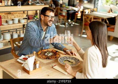 Deux personnes savourent leurs boissons à une table en bois, immergées dans une ambiance de restaurant détendue, tout en étant profondément dans la conversation et les rires. Banque D'Images