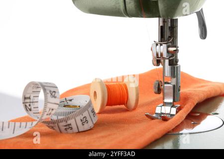 Machine à coudre avec tissu orange, ruban à mesurer et bobine de fil isolé sur blanc Banque D'Images