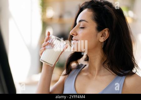 La jeune femme tient un verre de lait, les yeux fermés alors qu'elle savoure le goût Banque D'Images