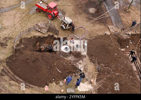 une équipe de plombiers effectue des travaux dans la rue pour remplacer les canalisations d’égout. Le tracteur a apporté un compresseur pour pomper l'eau du puits d'égout. Khark Banque D'Images