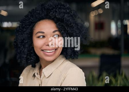 Jeune femme noire aux cheveux bouclés sourit tout en regardant par-dessus son épaule dans un cadre de bureau Banque D'Images