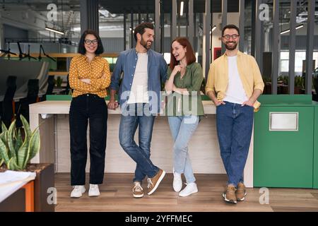 Quatre jeunes professionnels prennent une pause et parlent pendant la journée de travail dans un bureau moderne ouvert avec des éléments verts Banque D'Images