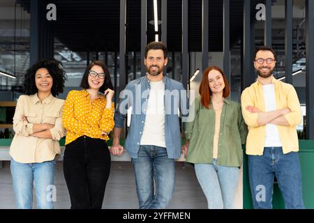 Cinq jeunes professionnels en vêtements décontractés sourient en s’appuyant sur un comptoir dans un bureau moderne Banque D'Images