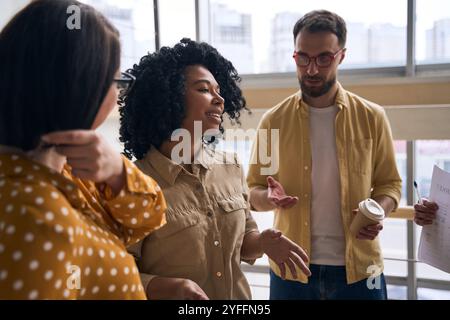 Une équipe diversifiée de collègues a une conversation informelle pendant une pause dans un bureau moderne, favorisant un environnement de travail positif et collaboratif Banque D'Images