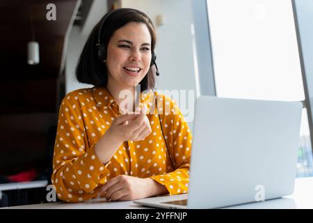 Femme d'affaires travaille avec joie à la maison, s'engageant dans une vidéoconférence avec des collègues, mettant en valeur la technologie moderne pour la communication à distance Banque D'Images