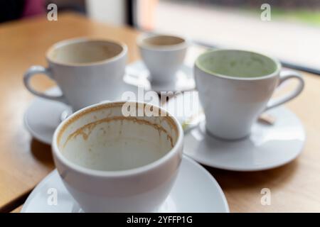 Quatre tasses à café vides avec des anneaux de résidus de café assis sur des soucoupes sur une table en bois Banque D'Images