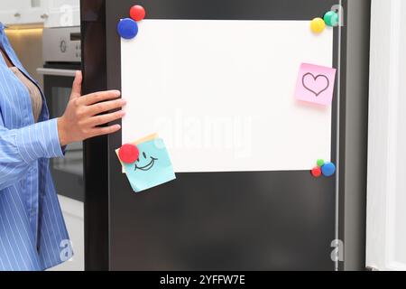 Femme ouvrant le réfrigérateur avec le tableau magnétique vierge et les notes dans la cuisine, gros plan Banque D'Images