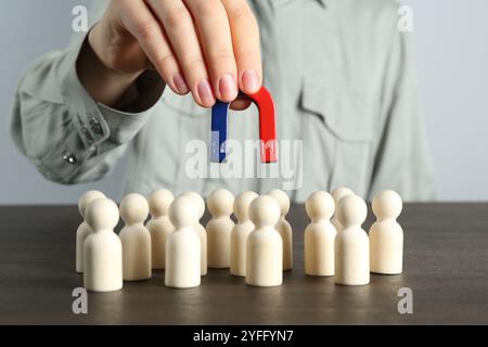 Femme avec aimant attirant des figures humaines à la table en bois, gros plan Banque D'Images