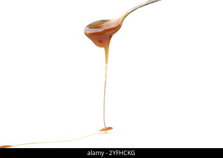 Sauce caramel savoureuse dégouttant de la cuillère sur fond blanc, gros plan Banque D'Images