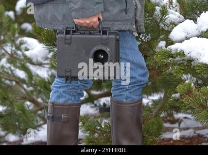 homme marchant dans une forêt enneigée, avec une gamecamera dans une valise à la main Banque D'Images