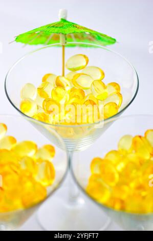 Macro de capsules de supplément d'huile de poisson oméga-3 servies en boissons sur trois verres à martini Banque D'Images