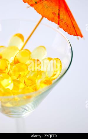 Macro de capsules de supplément d'huile de poisson de foie de morue dans un verre à martini sur fond blanc Banque D'Images