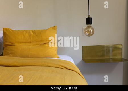 Chambre confortable avec literie moutarde et luminaire suspendu moderne, à la maison Banque D'Images
