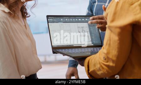Agent immobilier conseillant les clients sur le déménagement et la location de bureaux, examinant les plans détaillés et discutant de la conception architecturale de la nouvelle propriété. Négociation de contrat. Caméra B. Banque D'Images