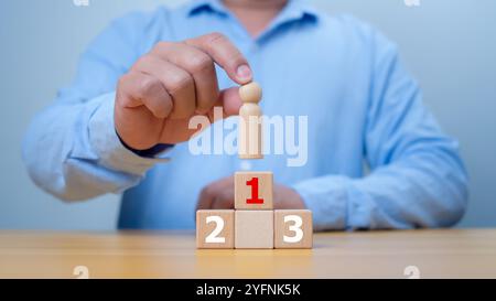 Hand Man place le dessus en bois de l'état ou le gagnant. Concept de succès, gagnant et victoire dans les affaires. Un homme tenant un modèle de personne en bois debout sur awar Banque D'Images