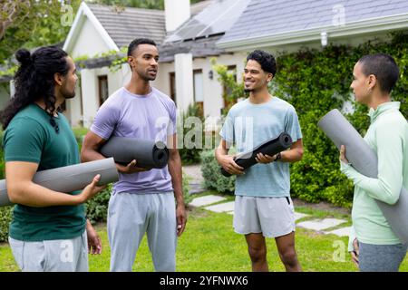 Jeunes amis multiraciaux tenant des tapis de yoga, discutant et souriant à l'extérieur dans le jardin Banque D'Images