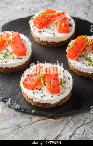 Sandwich, pain grillé avec saumon fumé, fromage à la crème, sésame et micro légumes verts pour un petit déjeuner sain en gros plan sur une assiette en ardoise sur la table. Vertical Banque D'Images