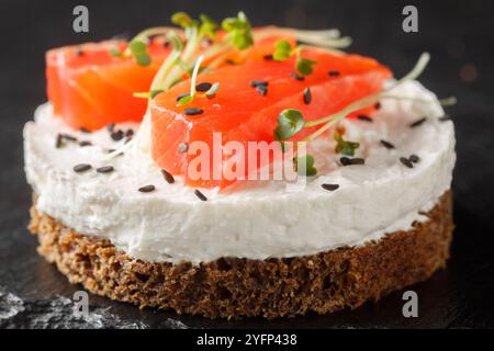 Sandwich danois traditionnel Smorrebrod avec pain de seigle noir, saumon, fromage à la crème, sésame et micro légumes verts pour un petit déjeuner sain en gros plan sur ardoise pla Banque D'Images