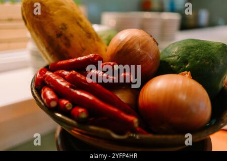Une exposition vibrante de piments rouges, d'oignons et de papaye verte disposés dans un panier tissé rustique, présentant des ingrédients frais et colorés parfaits pour Banque D'Images