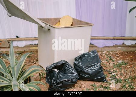 Une poubelle avec deux sacs poubelles noirs placés à côté, prêts à être éliminés dans un espace extérieur Banque D'Images