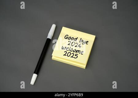 collez la note avec le texte manuscrit au revoir 2024 et bienvenue 2025 avec un stylo sur un fond noir Banque D'Images