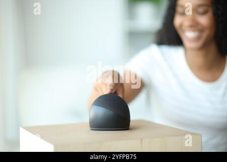 Femme noire heureuse utilisant une enceinte intelligente à la maison Banque D'Images