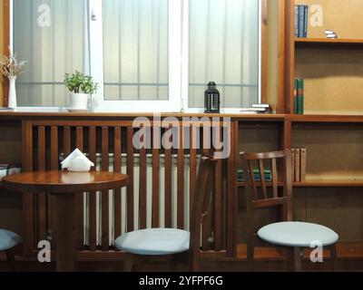 chaises et table près de la fenêtre à l'intérieur d'un café ou d'une pièce avec des livres sur les étagères, un lieu public pour étudier ou lire sans personne Banque D'Images