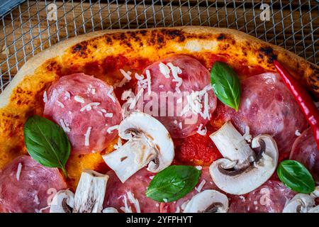 Pizza avec champignons, pepperoni , basilic et tomates sur une roue de cuisson. Gros plan. Photo de haute qualité Banque D'Images
