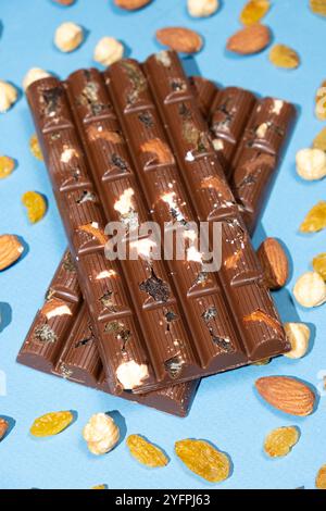 Barres de chocolat noisettes parmi les noix dispersées et les raisins secs sur un fond bleu. Banque D'Images