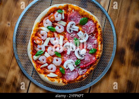 Pizza de deux moitiés : une avec pepperoni et champignons, l'autre avec crevettes et tomates. Pizza sur une roue de cuisson sur une table en bois. Espace pour le texte. Photo de haute qualité Banque D'Images