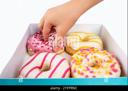 Vue latérale d'une main d'enfant atteignant pour saisir un beignet d'une boîte de quatre beignets multicolores Banque D'Images