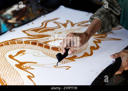 Production de batik. Femme utilisant de la cire chaude pour dessiner un dessin de dragon. Yogyakarta. Indonésie. Banque D'Images