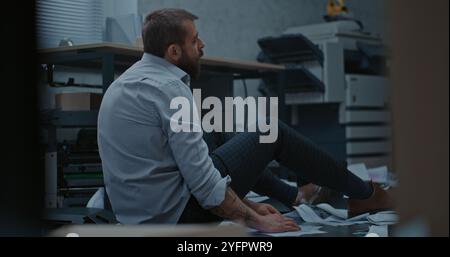 Homme d'affaires déprimé s'assoit sur le sol après la crise de rage sur l'affaire infructueuse. L'employé de bureau bouleversé respire fortement après avoir détruit la salle de bureau. Crise financière ou licenciement. Épuisement du travail. Banque D'Images