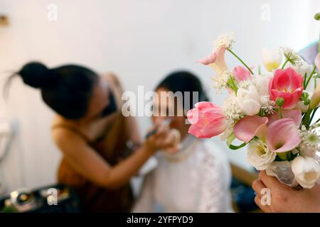 Mariée se préparant pour le mariage avec l'artiste de maquillage. Bouquet de fleurs roses blanches. Ho Chi Minh ville. Vietnam. Banque D'Images