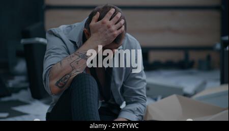 Nerveux et stressé employé de bureau respire fortement, s'assoit sur le sol après avoir détruit la salle de bureau. Homme d'affaires frustré après l'échec d'un accord commercial ou recevoir de mauvaises nouvelles. Crise financière. Épuisement du travail. Banque D'Images