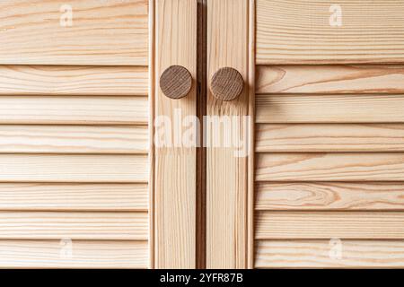 Portes à persiennes en bois avec poignées de bouton en bois gros plan. Les portes à persiennes de la cuisine extérieure sont faites de bois de pin léger avec un motif de grain naturel Banque D'Images