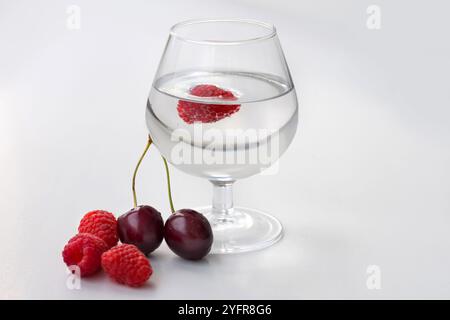 Baies fraîches, cerises, framboises sur fond blanc. Framboises dans un verre Banque D'Images