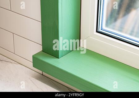 Fragment de fenêtre en plastique avec rebord de fenêtre en bois vert et cadre en bois sur fond carrelé blanc vue rapprochée Banque D'Images