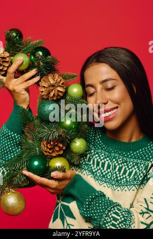 Une jeune femme joyeuse tient une belle guirlande ornée d'ornements, souriant brillamment. Banque D'Images