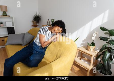 Jeune fille afro-américaine faisant une sieste paisiblement sur un canapé jaune à la maison Banque D'Images