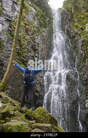 Tourist attraction of Germany, falls of Burgbach Waterfall near Schapbach, Black Forest, Baden-Wurttemberg, Germany. Man hiker in blue jacket standing Banque D'Images