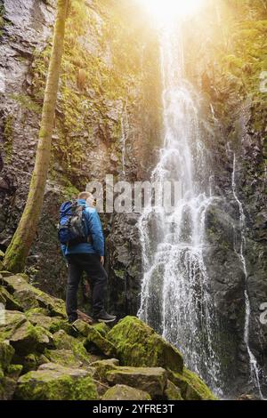 Tourist attraction of Germany, falls of Burgbach Waterfall near Schapbach, Black Forest, Baden-Wurttemberg, Germany. Man hiker in blue jacket standing Banque D'Images