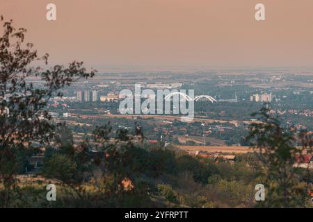 Vue aérienne de Novi Sad avec le pont emblématique sur la rivière, avec l'horizon et l'architecture de la ville illuminés par un lever de soleil époustouflant Banque D'Images