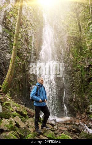 Tourist attraction of Germany, falls of Burgbach Waterfall near Schapbach, Black Forest, Baden-Wurttemberg, Germany. Man hiker in blue jacket standing Banque D'Images
