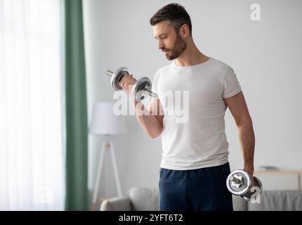 Gros plan de beau barbu homme faisant l'entraînement de haltères à la maison Banque D'Images