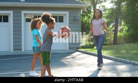 Mère et enfants jouant au basket-ball à l'extérieur sur l'allée à la maison Banque D'Images