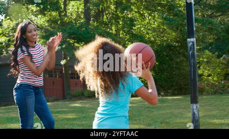 Mère et fille jouant au basket-ball à l'extérieur sur l'allée à la maison Banque D'Images